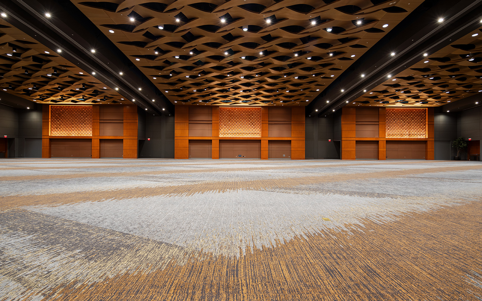 Ground level photo taken of a modern ballroom with warm wood accents, intricate ceiling design, and versatile event lighting.