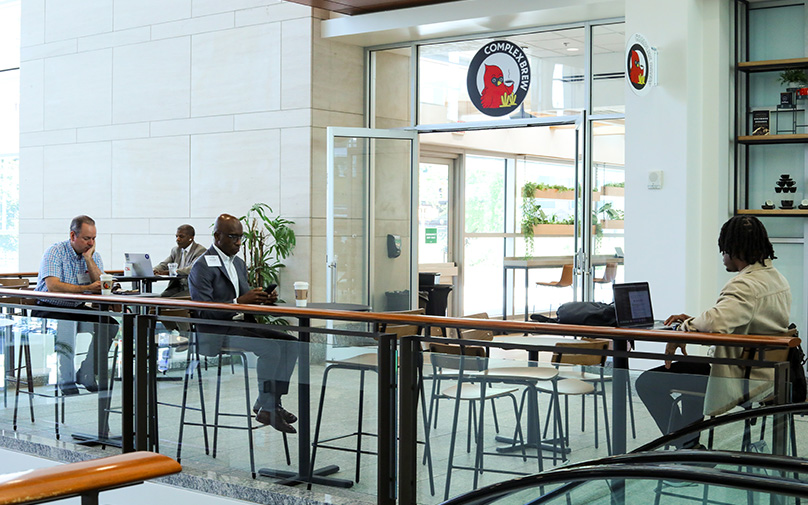 Four individuals pictured working, sitting at their tables in the seating area outside of the coffee shop.