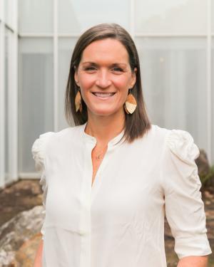 Headshot of Emily Dunn smiling and wearing a white top and dangling earrings.