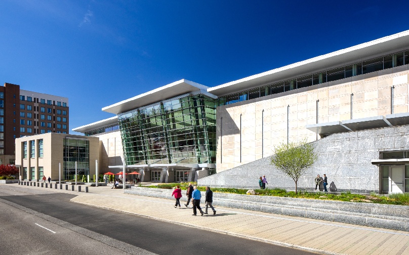 View of the entrance to Atlantic Union Bank Convention Center from the side with people gathered and sitting at tables with red umbrellas.