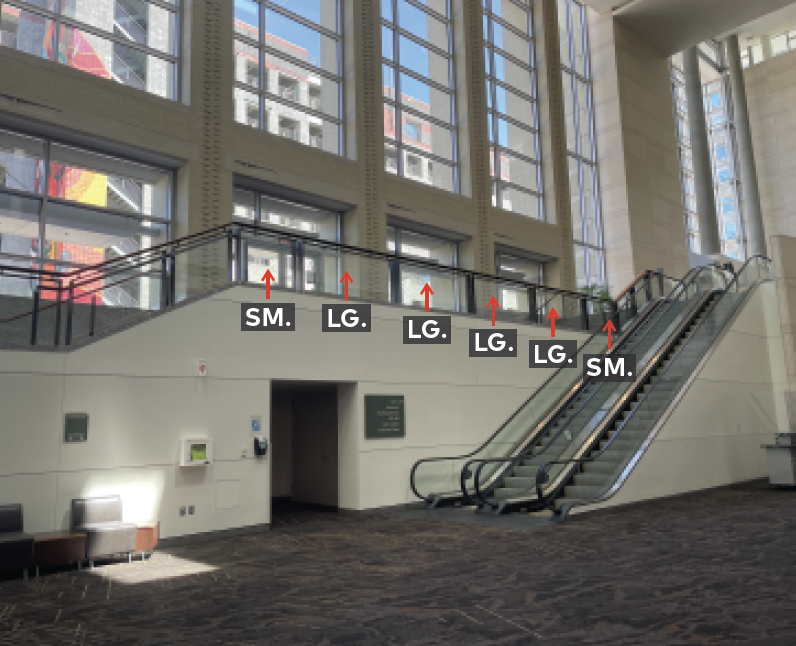 Upper mezzanine landing with railing and glass panels. Next to escalator.
