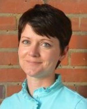 Headshot of Trish LaPaglia standing in front of a brick wall smiling with a closed mouth wearing a light blue top.